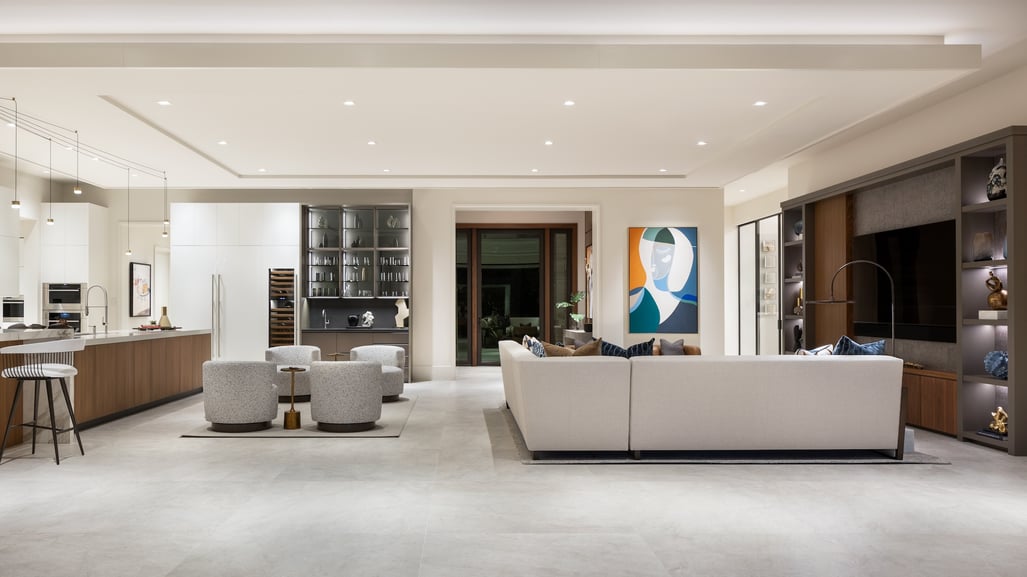 Luxury living room and open-concept kitchen featuring custom cabinetry, neutral furnishings, built-in shelving, and contemporary interior design by Romanza.