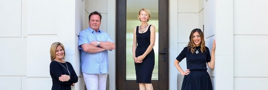 three women and one man posing in front of a brown front door of a house