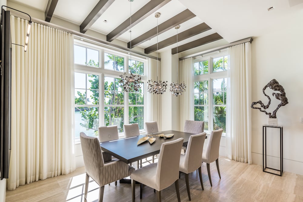 dining room with brown table and eight white chairs around it, white curtains opened to show windows and yard
